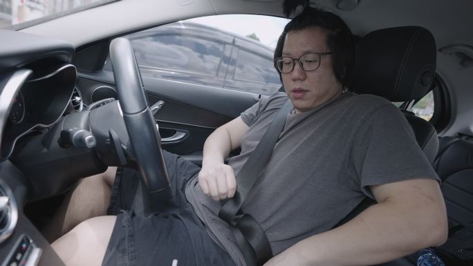 一名亚洲年轻男子上车，系好安全带，开车回家。