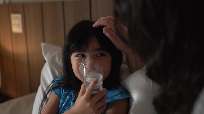 母亲在家中的床上帮助女儿使用喷雾器进行吸入治疗