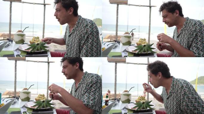 一名白人男子在海滩上的餐厅吃菠萝泰式甜点