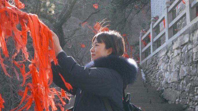 中国陕西，一名女子在寺庙的手杖上系着红丝带。