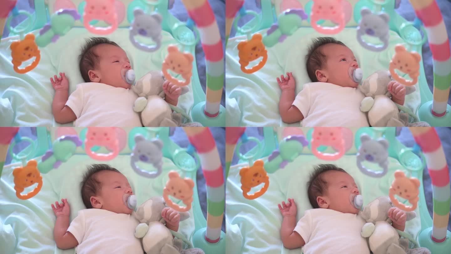 睡意朦胧的40天大的新生男婴躺在床上准备小睡，卧室里的玩具挂在他身上