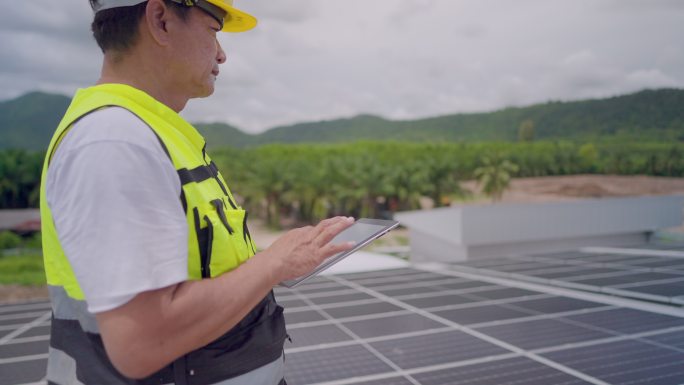 穿着安全制服的亚洲工程师或承包商，检查项目进度，并将太阳能发电厂的太阳能电池板安装在建筑物屋顶的平板
