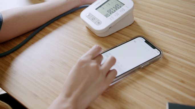 POV：亚洲女性在家中使用智能手机记录血压监测仪上的自我血压和心率数据