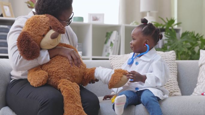 4k视频画面显示，一个小女孩穿着医生服装，与母亲和泰迪熊在家玩耍