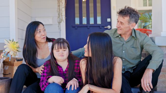 多样化的家庭坐在家门口。一个女儿患有唐氏综合症。