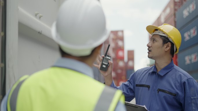 专业的亚洲工程师，向主管或合作伙伴解释集装箱维护系统，以及在港口装卸场从货运船上装载进出口集装箱。物