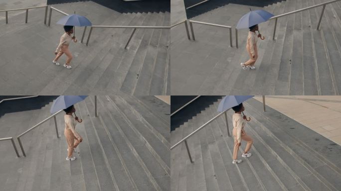 一位年轻迷人的深肤色女商人，身穿米色服装，打着伞，从高处俯瞰，走上楼梯