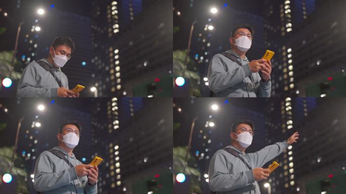 亚洲中国中年男子戴着口罩，在晚上用手机应用程序在线预订后，在城市里举起双臂叫众包出租车