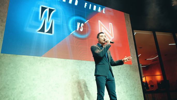 亚洲华人Emcee电子竞技比赛节目主持人在舞台上用背景投影屏幕介绍盛大的最终电子游戏比赛