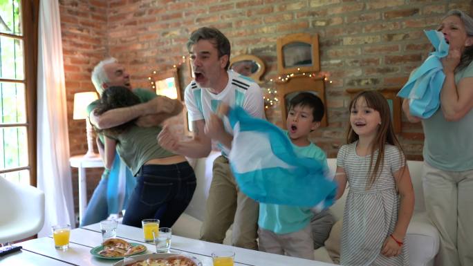 阿根廷家庭足球迷兴高采烈，尖叫着吃着外卖披萨，看着足球比赛