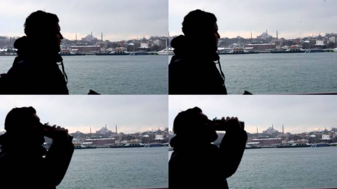 一个男人在船上旅行的剪影，对着索菲亚大教堂的景色喝咖啡，从游轮上观看壮丽的城市景色，男人在船的封闭空