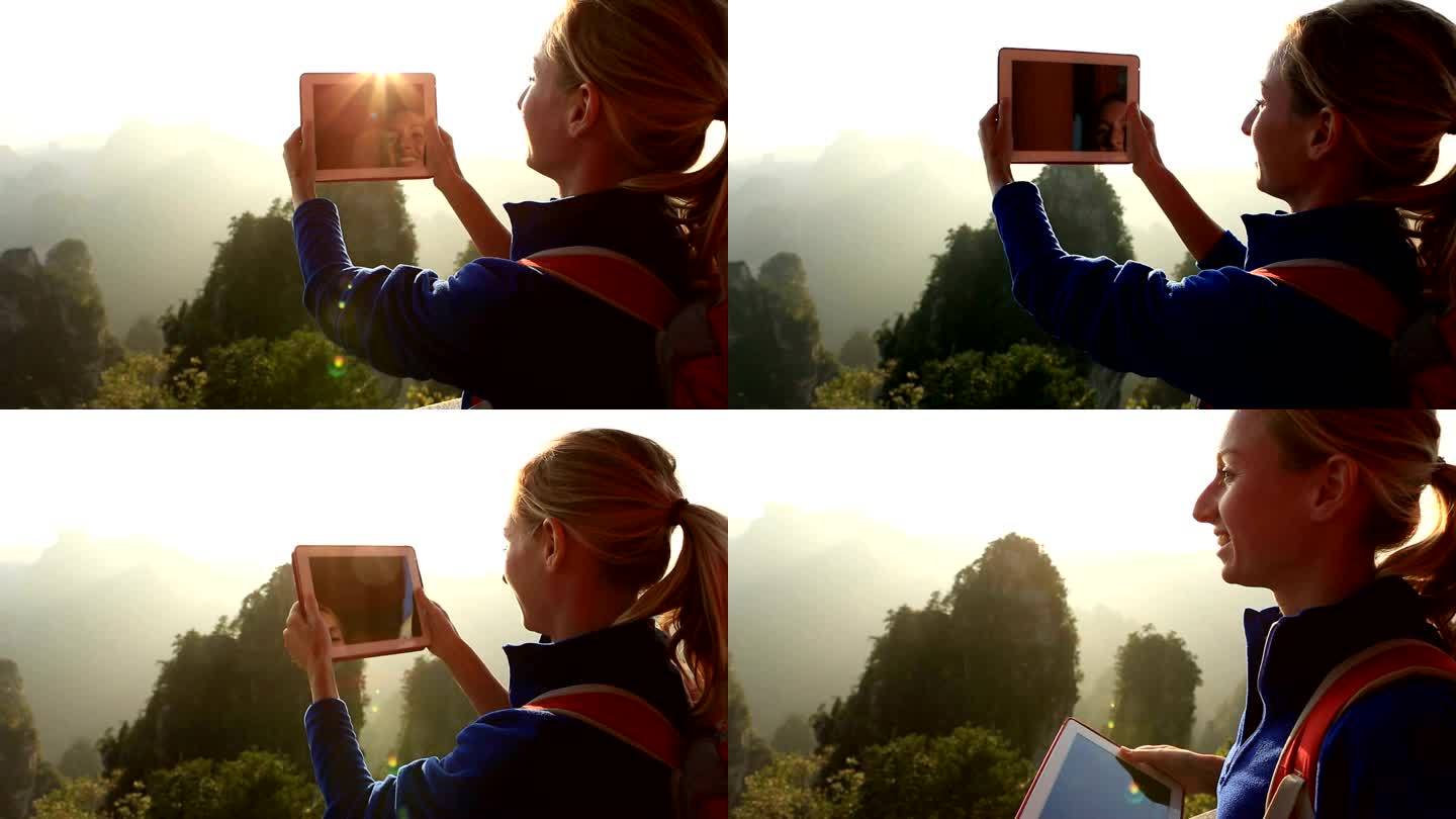 女登山者在山顶拍摄数码平板电脑照片