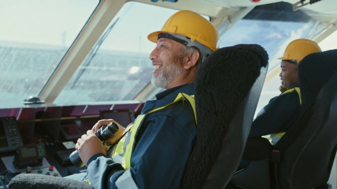 船上的两名男子手持望远镜值班。穿着黄色背心和安全头盔的快乐机械师坐在一艘俯瞰大海的商船前