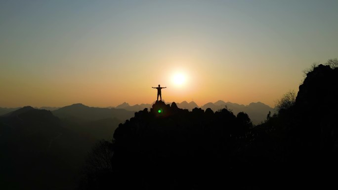 男人登山成功山顶张开双臂拥抱太阳眺望远方
