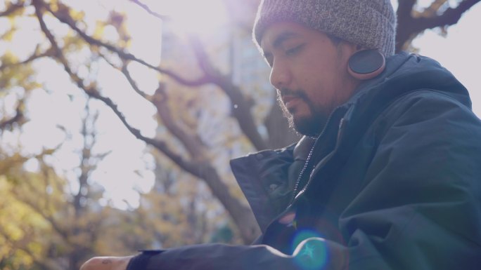 一名留着胡须的亚洲男子手持智能手机，在日落时分拍照。