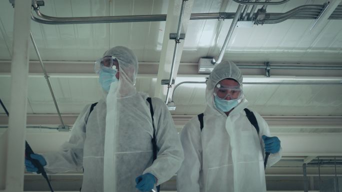 两名男性专家穿着防护服和面罩，在办公室和病原体繁殖地进行消毒，4K分辨率，新冠肺炎影响，