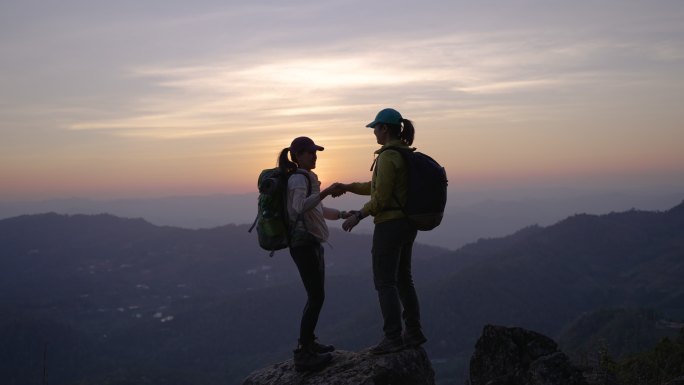 两名女子徒步登山，在山顶击掌，并举起双手庆祝成功