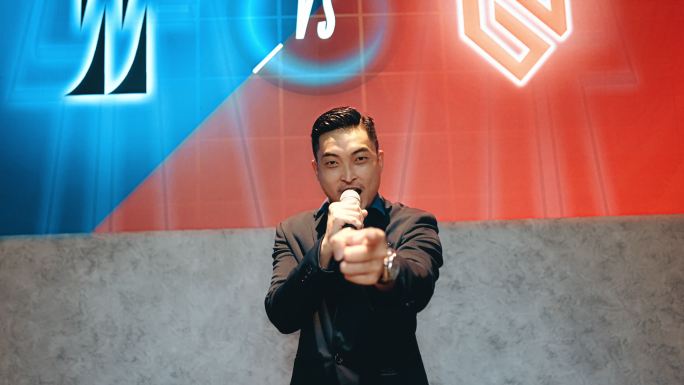 亚洲华人Emcee电子竞技比赛节目主持人在舞台上用背景投影屏幕介绍盛大的最终电子游戏比赛