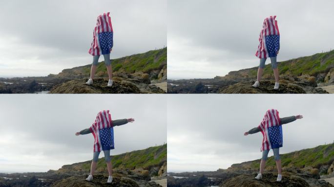 太平洋狂野海岸的岩石上挂着美国国旗的女人。加利福尼亚