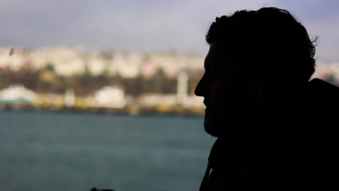 一个男人在船上旅行的剪影，在伊斯坦布尔博斯普鲁斯海峡的景色下喝咖啡，从游轮上观看壮丽的城市景色，在船
