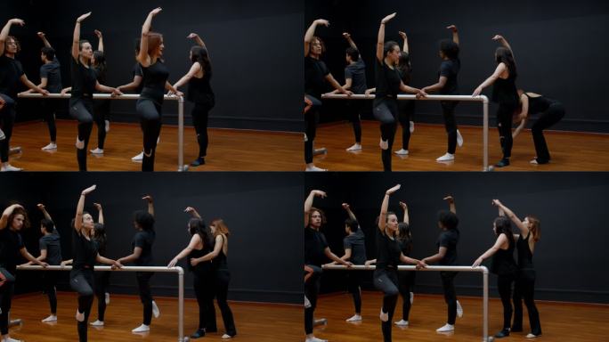 女芭蕾舞老师向全班展示正确的姿势，然后在学生们抓住双杠的时候绕着他们纠正