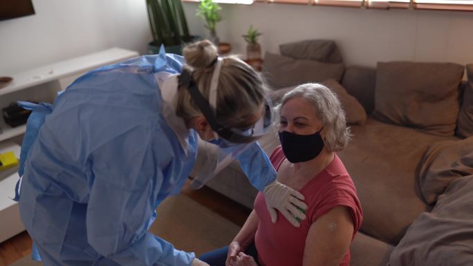 医生在家里给一位情绪激动的老年妇女贴上了“Fui vacinado”（接种疫苗）贴纸——戴着口罩