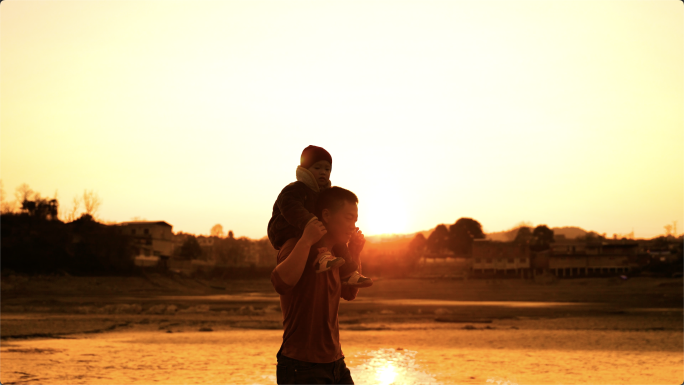 父亲和儿子，儿子骑在父亲肩膀上走在夕阳下