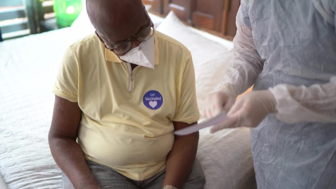 医生在家中为老年男子颁发免疫疫苗证书-戴口罩