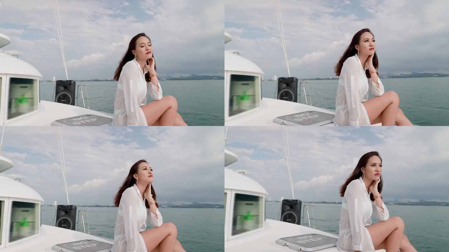 一位美丽的亚洲女性，棕色长发，白色束腰外衣，在海上航行时，她坐在游艇鼻子上，摆出姿势，享受着海上航行