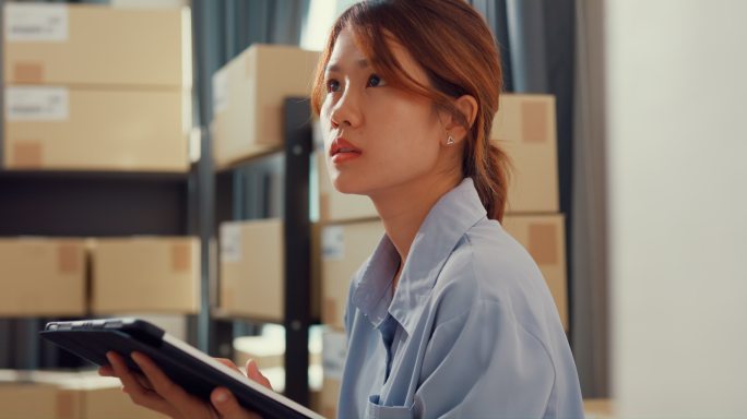 站在货架前的亚洲女商人使用数字平板电脑检查货架上的库存，并在仓库快递前详细查看在线信息中的关键数据。