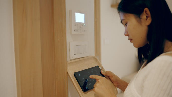 亚洲女性用家庭自动化和智能家居技术打开空调、电灯和空调。