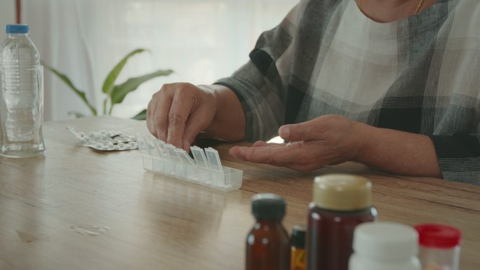 一位老年妇女从放在家里的每日药片整理盒中的药袋中取出药物，然后合上盖子。