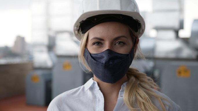 一名工厂的女工程师戴着防护头盔和面罩面对摄像头
