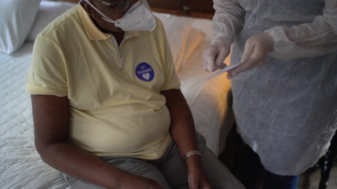 医生在家中为老年男子颁发免疫疫苗证书-戴口罩