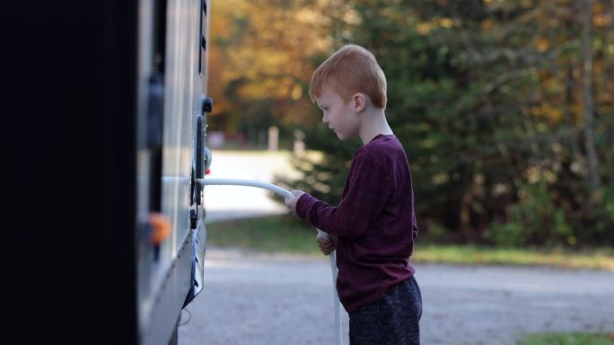 加拿大魁北克省秋季露营地上，小男孩将水管连接到露营拖车上