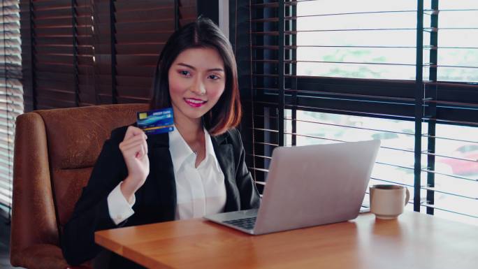 20-30岁的亚洲女性穿着西装，举着Moc k up展示模拟信用卡的例子。桌子上放在电脑旁边。Con