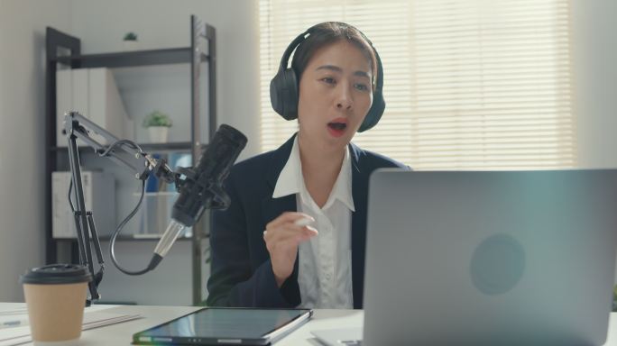 年轻的亚洲女商人在录音室的笔记本电脑上录制和广播播客。