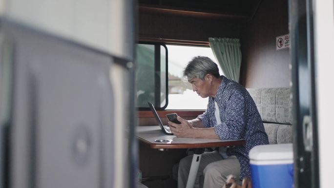 度假期间，亚洲中国老年男子早上在露营车上用笔记本电脑打字