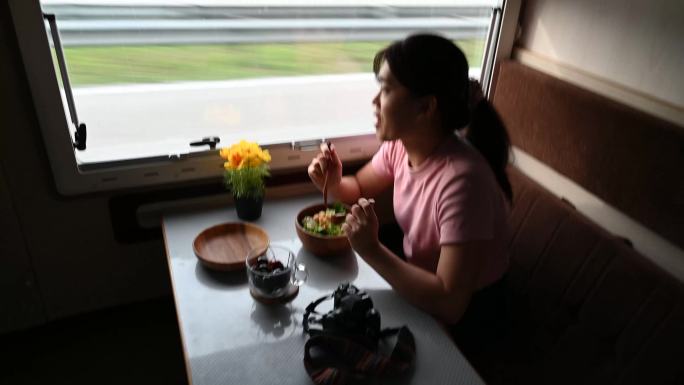 从侧面车窗向外看，年轻的亚洲女性喜欢在车里吃沙拉早餐。露营车旅行系列