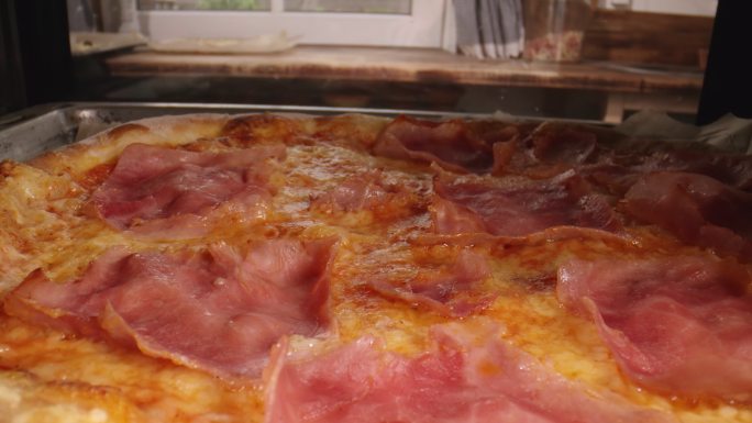 在家庭厨房用火腿和新鲜罗勒制作披萨