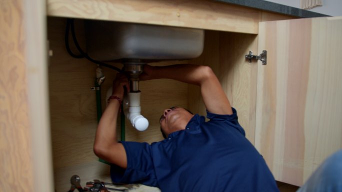 拉丁美洲水管工在顾客家中的厨房水槽下安装水管