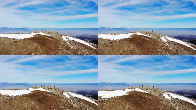 无人机鸟瞰登山队双臂交叉站在一座岩石山的山顶上观看风景。