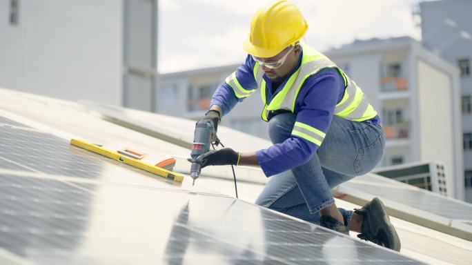 一名年轻人在楼顶安装太阳能电池板时，使用钻头、卷尺和水准仪。一名男子在可再生能源建筑项目中使用工具