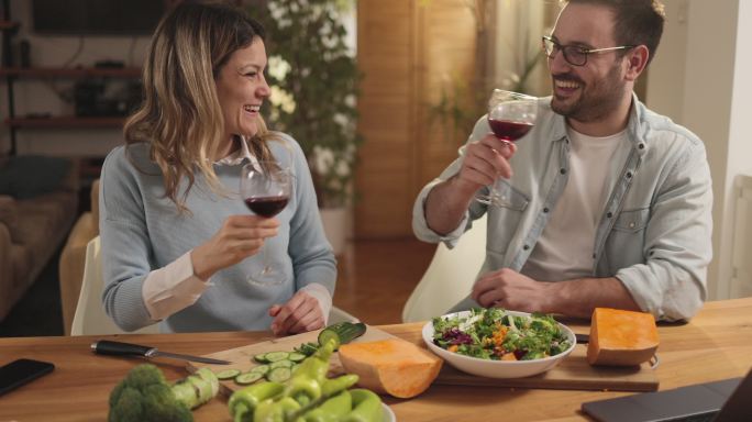 幸福的夫妇一边在家里做健康的饭菜一边敬酒。