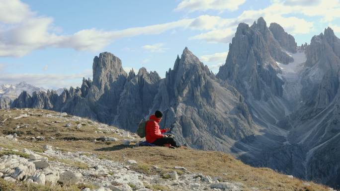 日落时，男性旅行者和他的狗一起休息，欣赏阿尔卑斯山脉的风景