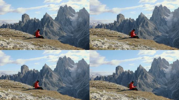 日落时，男性旅行者和他的狗一起休息，欣赏阿尔卑斯山脉的风景