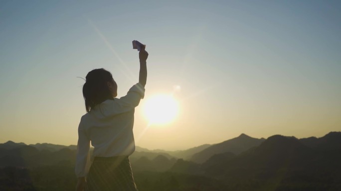 女生站在山顶扔纸飞机美女背影放飞梦想希望