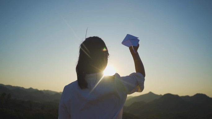 美女山顶逆光背影扔纸飞机白衬衫女生站山顶