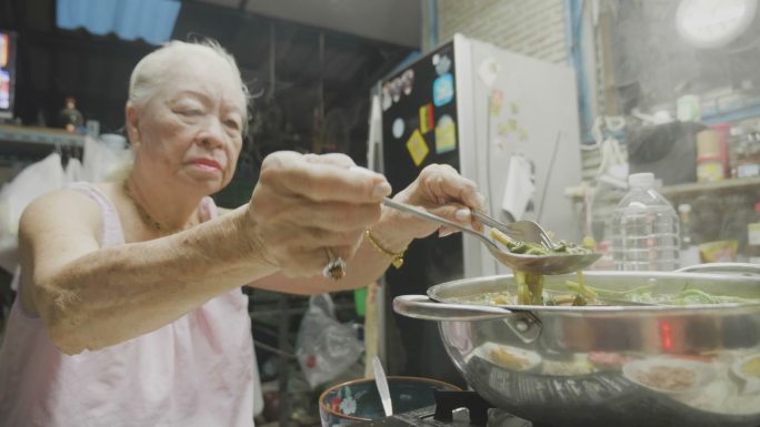 高级亚洲女性在电锅里煮着萝卜、排骨、鱿鱼、玉米、粉丝和猪肉，吃着苏基或沙布。概念：爱、食物、亚洲食物