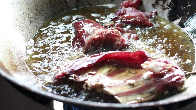 近景是在一个旧平底锅里炸大块牛肉。